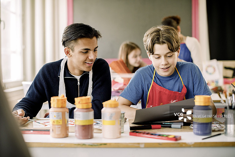 高中绘画课上，青少年男孩向男性朋友展示画作图片素材