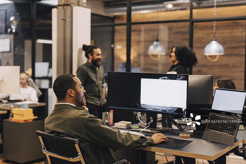 办公室里，男职员在办公桌前使用电脑的背影图片素材