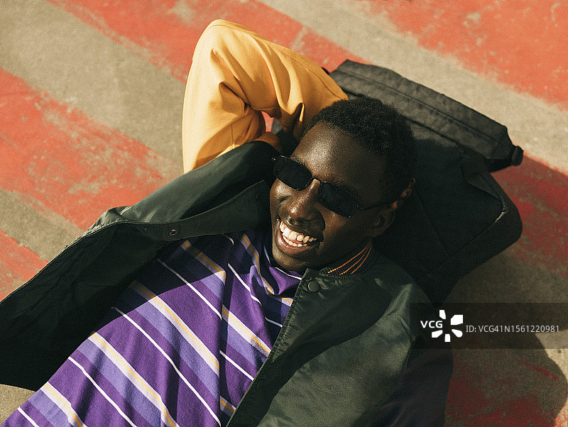 在阳光明媚的日子里躺在地板上戴着太阳镜的快乐年轻人图片素材