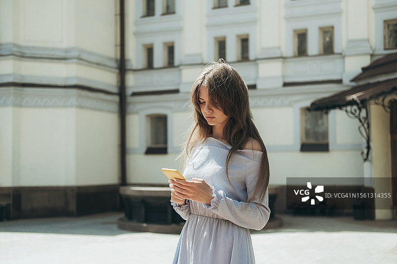 年轻女人在晴天里靠在建筑物旁使用智能手机图片素材