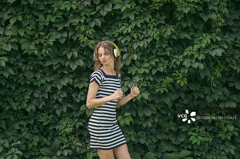 靠在绿墙边跳舞听音乐的年轻女子图片素材