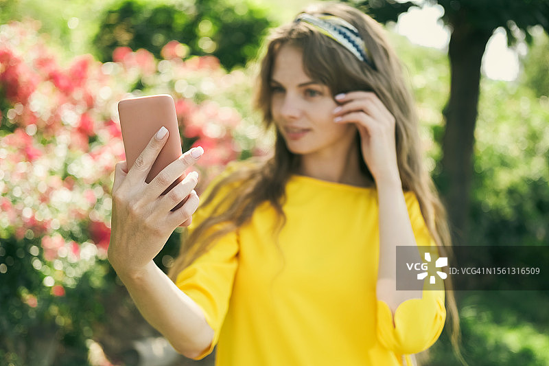 年轻女人在户外对着红色鲜花和树木自拍图片素材