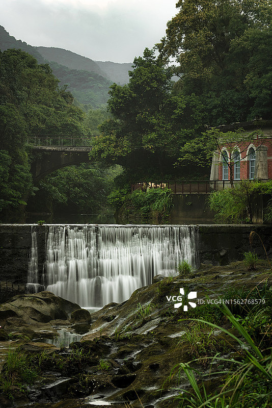山区里的小型水坝，带有一座红砖建筑和桥梁图片素材