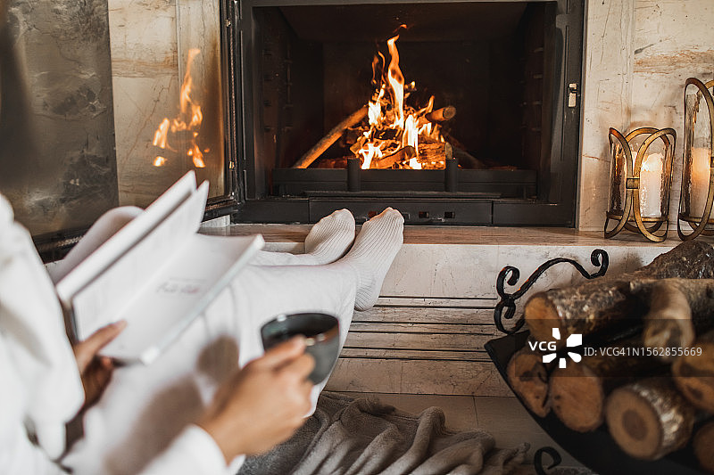 女子手拿咖啡和书坐在壁炉旁图片素材