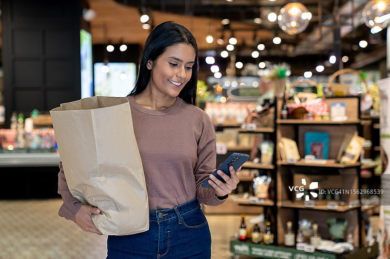 女人离开超市，提着购物袋查看手机图片素材