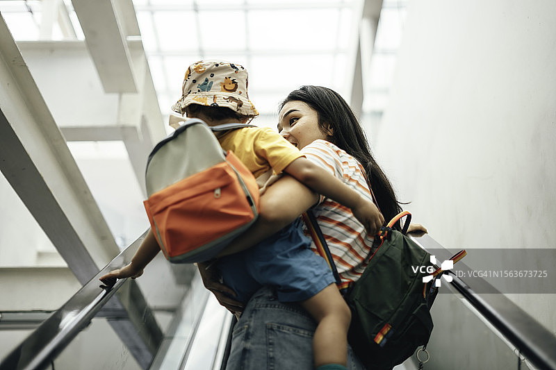 母亲和儿子背着背包乘坐自动扶梯去上学图片素材