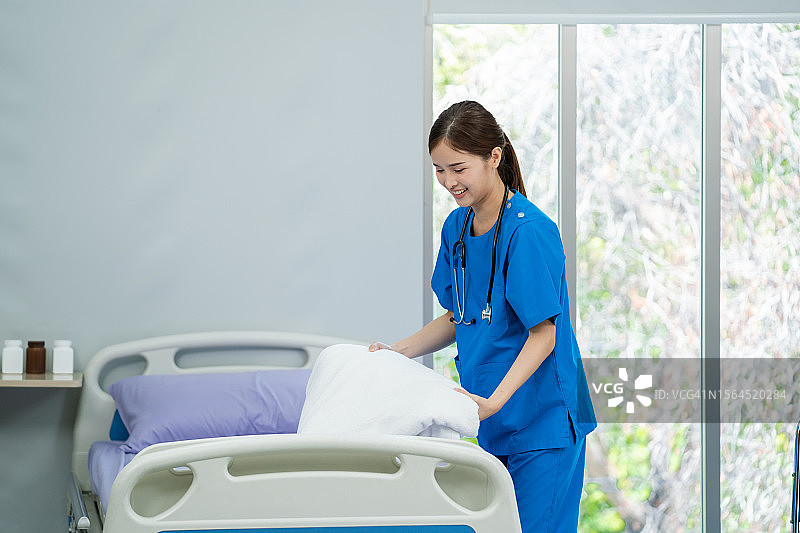 穿蓝色制服的女护士在医院病房更换病床床单，医疗保健概念图片素材
