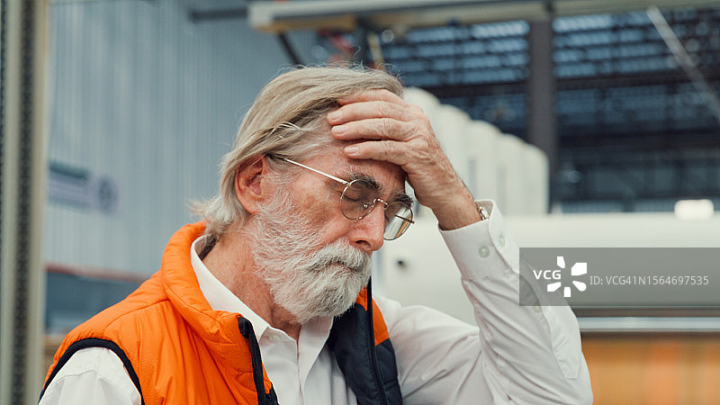 疲惫的专业男工业工程师在制造工厂摘下头盔，在制造工厂或生产车间工作图片素材