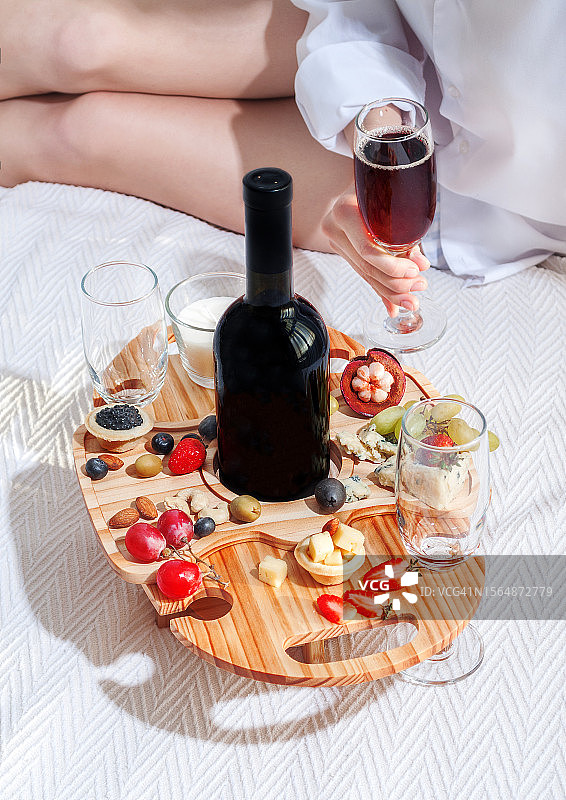 年轻女人手持葡萄酒杯，在床上享用浪漫早餐图片素材