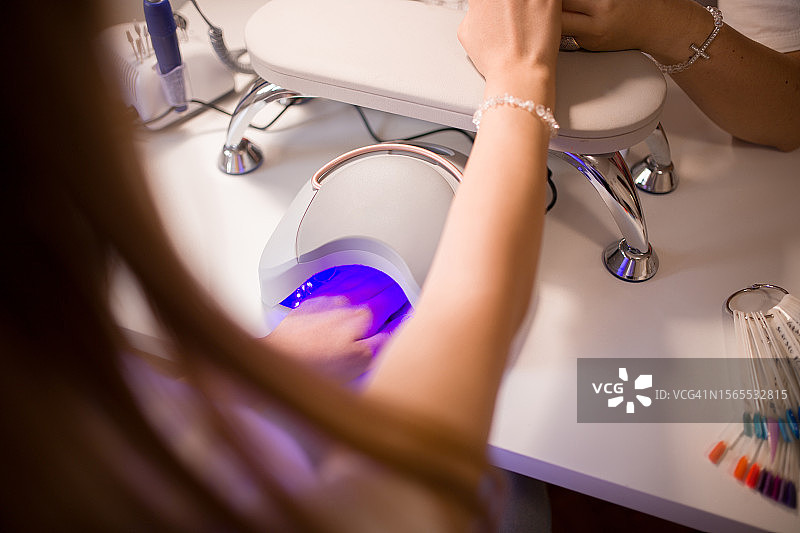 美甲师用紫外线灯为年轻女士做美甲图片素材