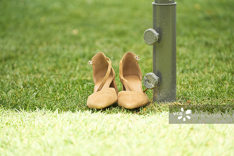 公园草地上靠着柱子的空女士高跟凉鞋特写，正面视角图片素材