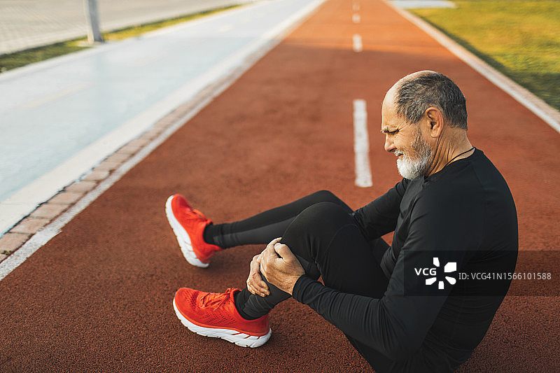 在跑道上痛苦地抱着受伤腿部的老年男人，健康问题图片素材