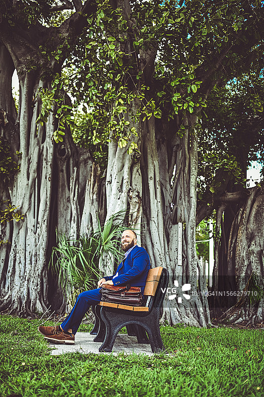 身穿商务西装的男人坐在户外长椅上，可能在等公共交通或休息图片素材