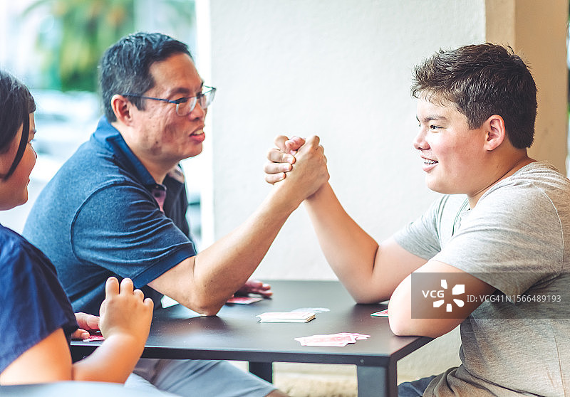 华裔美国父亲与青少年儿子友好地掰手腕图片素材