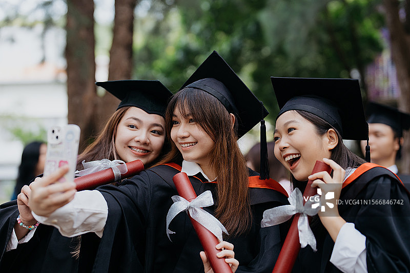 亚洲女学生穿着毕业礼服，用智能手机自拍图片素材