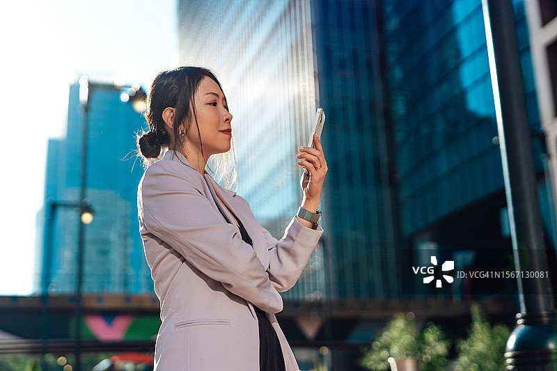 自信的亚洲女商人在现代办公楼使用智能手机图片素材