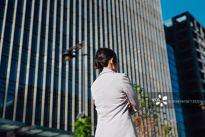 自信的亚洲女商人在现代办公楼前叉腰的背影图片素材