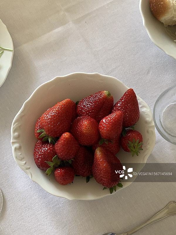 亚麻桌布上的有机新鲜红草莓碗，配有精致的银器。2022年5月意大利豪华酒店的豪华早餐桌图片素材