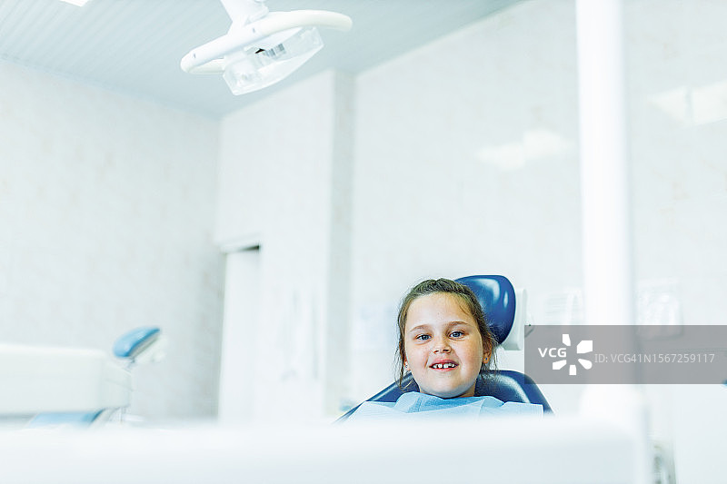 快乐的小女孩坐在牙科诊所里，等待接受系带切除手术图片素材