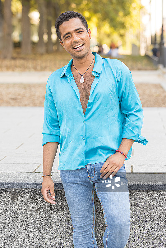 在城市里享受空闲时光的，穿蓝色衬衫和牛仔裤的棕发拉丁裔男人图片素材