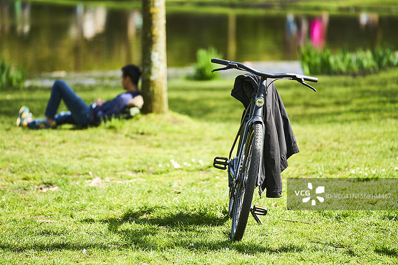 停在公园草地上的自行车，背景中一个男人躺在树旁图片素材