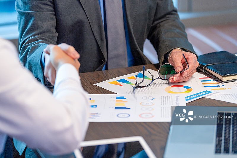 商务人士握手，身穿商务服装，有包含财务图表的文书图片素材