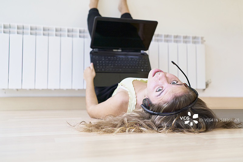 十几岁的女孩躺在地板上用电脑，脚放在墙上的正面照图片素材