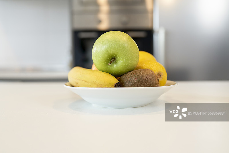 装有水果的白色陶瓷盘，绿苹果，香蕉在桌子上，背景模糊图片素材