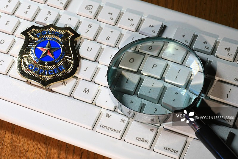 电脑键盘上的警察徽章和放大镜图片素材