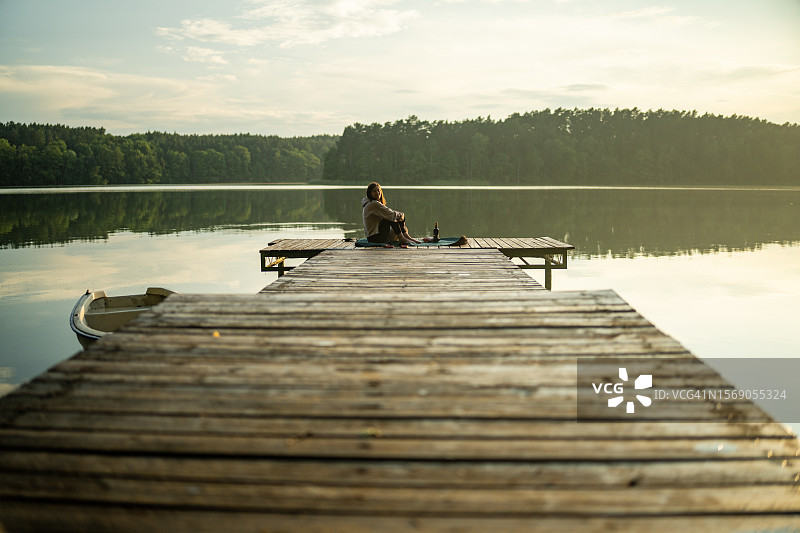 女人在木质码头放松，看着平静水面图片素材