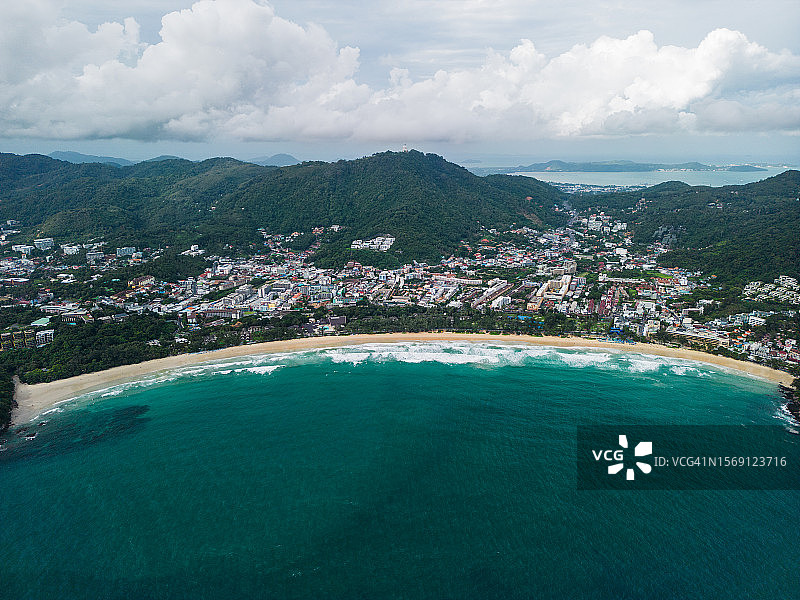 普吉岛卡塔海滩鸟瞰图，有许多游客和驾驶摩托艇的游客，以及带有绿色山地建筑的芭东镇图片素材