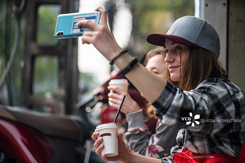 年轻女子与朋友坐在路边喝咖啡自拍图片素材