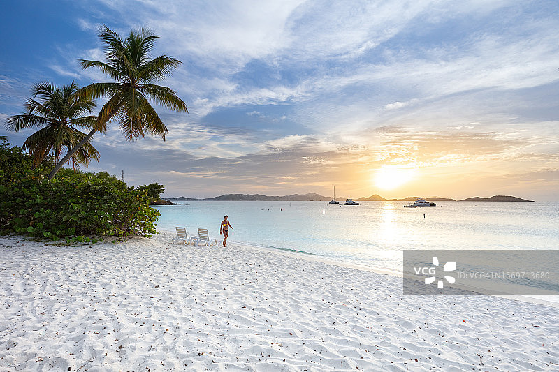 热带海滩上躺椅和棕榈树旁的比基尼女人图片素材