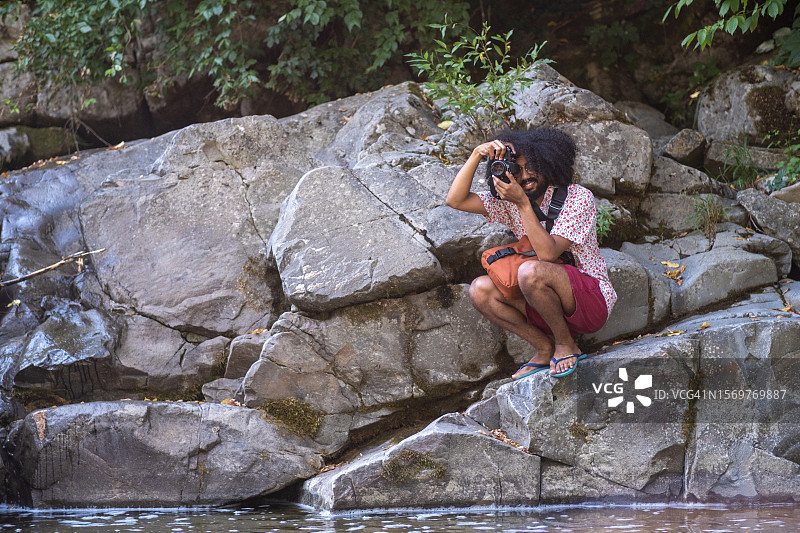 一位年轻的非裔美国男子在河边的岩石上拍照图片素材