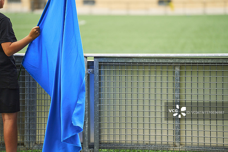 男孩身穿运动服站在足球场上，手持蓝色旗帜，后视图图片素材