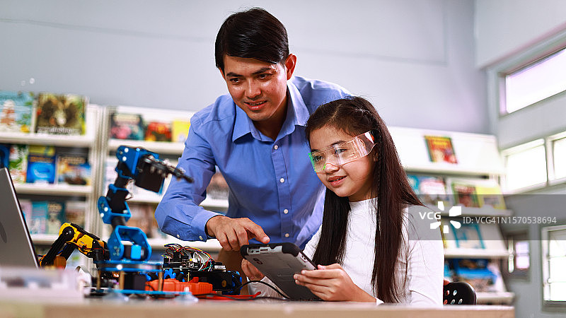 一位年轻有创意的男老师向学生们讲解机器人机器的工作原理，同时手持游戏手柄。科学与教育。儿童的发明和创造力。图片素材