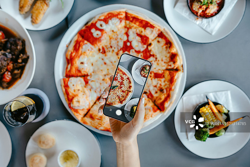 女人在最喜欢的餐厅用智能手机拍摄餐桌上的午餐，并在吃之前分享到社交媒体的俯视角度照片。相机先吃文化。分享食物。人物、食物、生活方式和技术图片素材