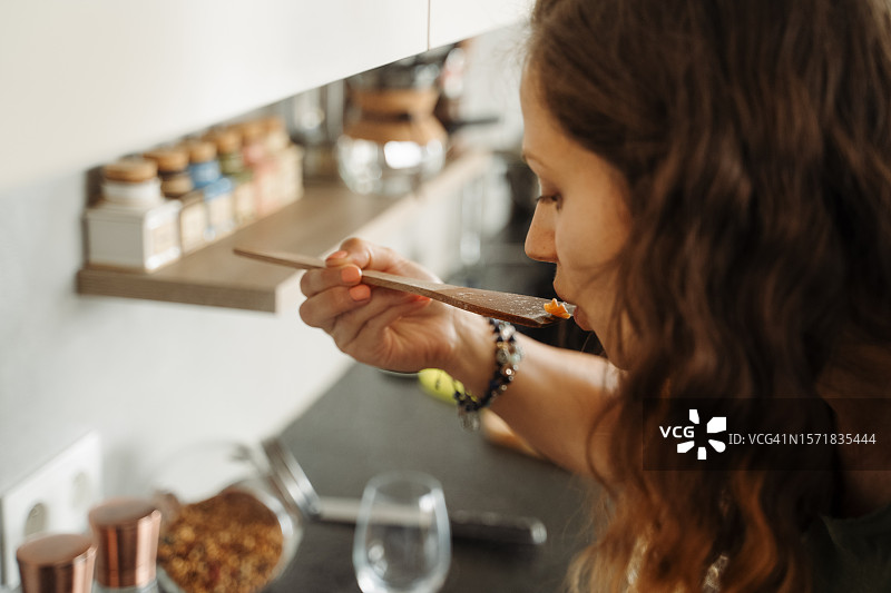 女人在现代厨房烹饪素食，用木勺品尝意大利面图片素材