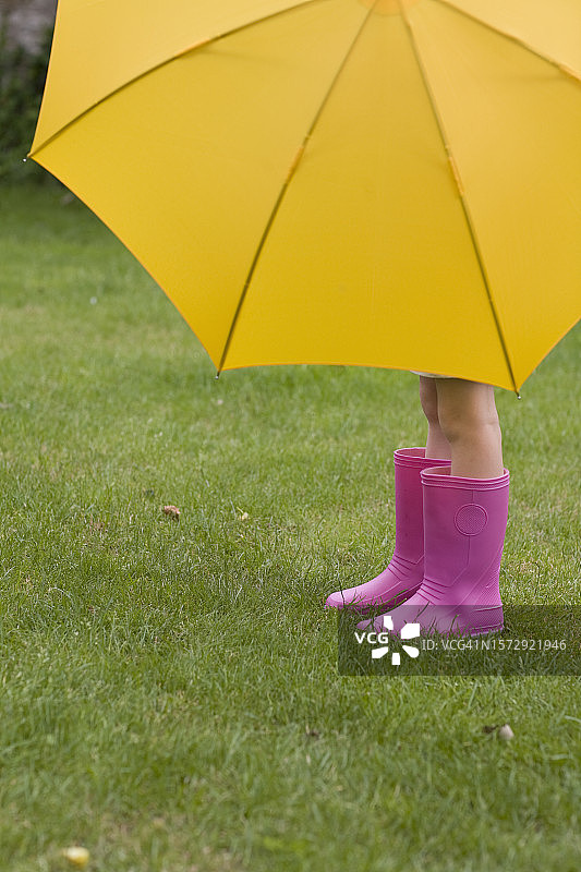 在黄色雨伞下穿着粉色靴子的年轻女孩图片素材