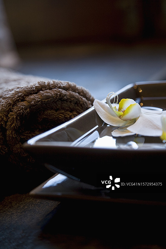 漂浮在方形碗中的白色花朵与棕色毛巾图片素材