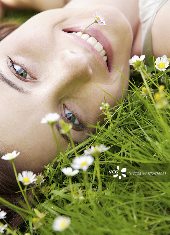 年轻女人躺在鲜花盛开的田野上，嘴里叼着雏菊图片素材