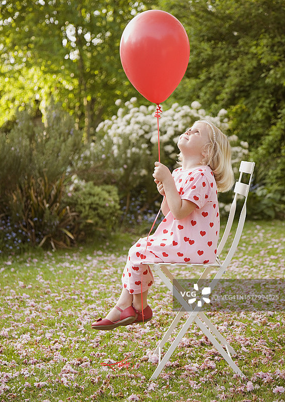 坐在花园椅子上拿着红色气球的年轻女孩图片素材