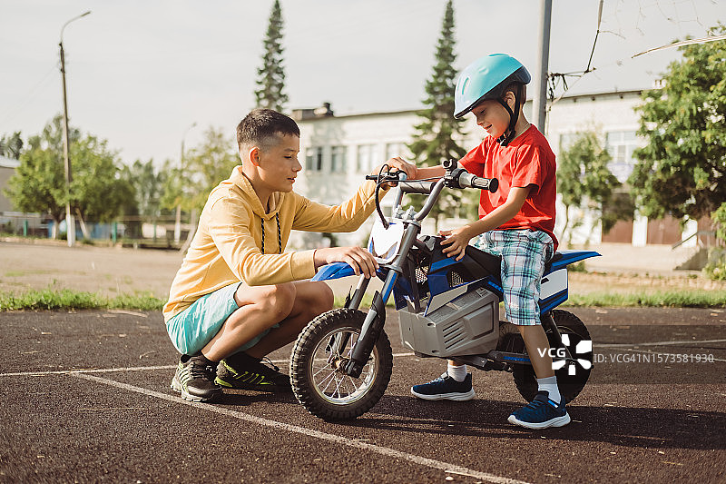 青少年男孩教弟弟骑电动摩托车，夏季学童健康的户外运动图片素材
