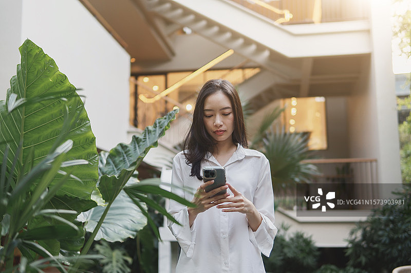 亚洲女性在花园家具上放松，使用手机进行商务沟通图片素材