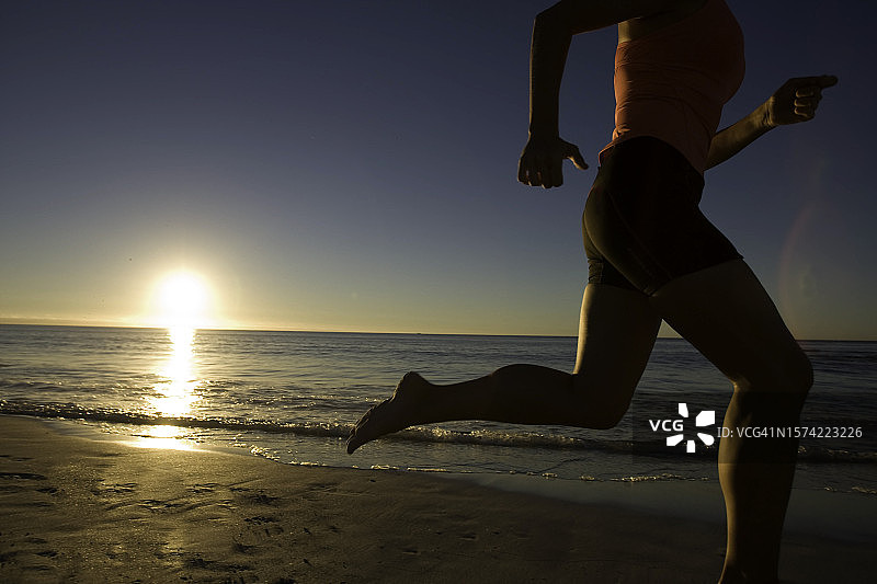 日落时分年轻女人在海滩上奔跑图片素材