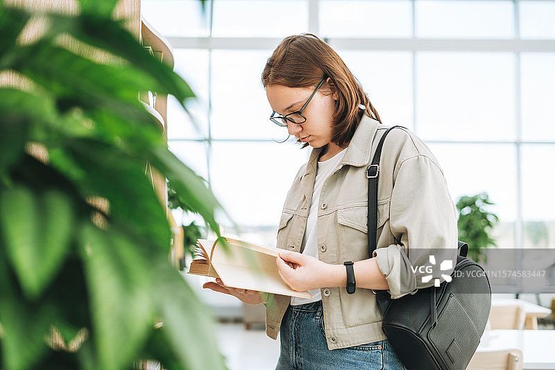 戴眼镜的少女在现代图书馆用手机图片素材