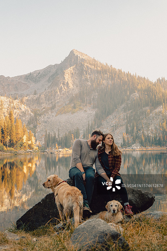 年轻夫妇与宠物金毛在湖边岩石上享受家庭时光风光照（美国爱达荷州麦考尔）图片素材