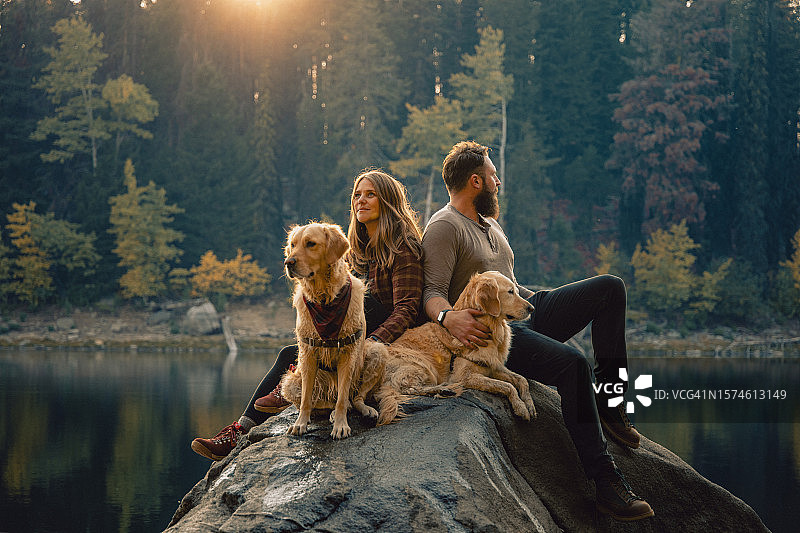 年轻夫妇与宠物金毛在湖边岩石上享受家庭时光风光照（美国爱达荷州麦考尔）图片素材