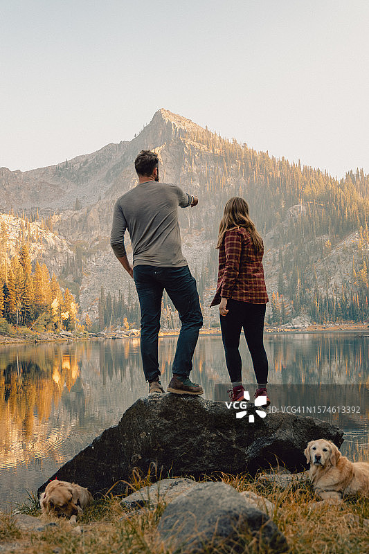 美国爱达荷州麦考尔：年轻夫妇与宠物金毛犬在湖边岩石上享受家庭时光图片素材