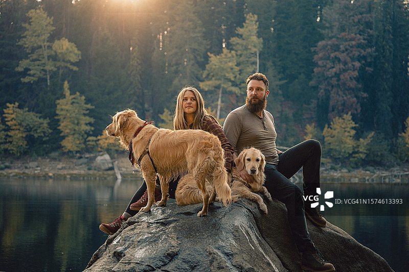 年轻夫妇与宠物金毛在湖边岩石上享受家庭时光风光照（美国爱达荷州麦考尔）图片素材